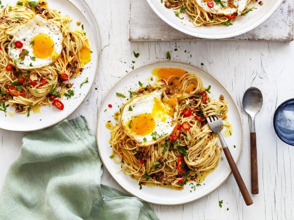 a fried egg atop a bed of thin noodles, garnished with herbs and chilli