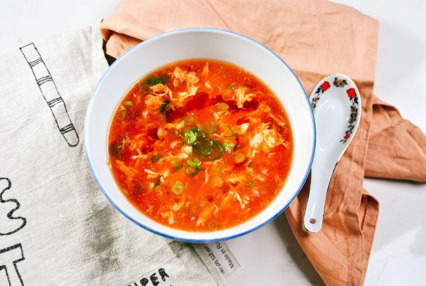 tomato egg drop soup in a white bowl with a soup spoon on the side